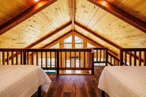 A cozy attic bedroom with wooden beams, a balcony, and a large window. - Treetop Oasis on the crystal clear Nueces River in the Texas Hill Country (UVALDE)