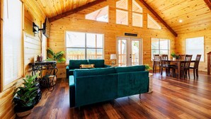 A spacious wooden cabin with a high ceiling, a cozy green sofa, a dining area, and large windows allowing natural light.