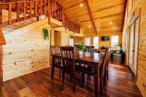 A wooden cabin interior with a dining area, staircase, and a cozy living space. - Treetop Oasis on the crystal clear Nueces River in the Texas Hill Country (UVALDE)
