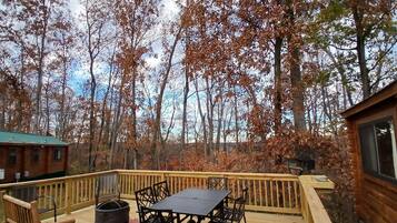 A wooden deck with a table and chairs, a fire pit, and a view of a forested area.