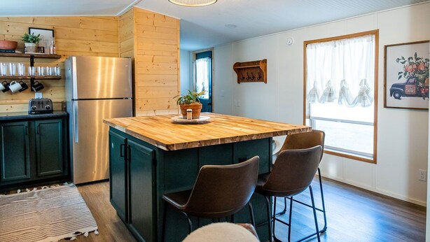 A kitchen with a wooden island, two bar stools, a stainless steel refrigerator, and a hanging light fixture. -  Lake Rathbun Get Away  (Rathbun)