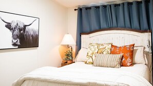 A neatly made bed with a white duvet, a headboard with a floral pattern, and a blue curtain. -  Lake Rathbun Get Away  (Rathbun)