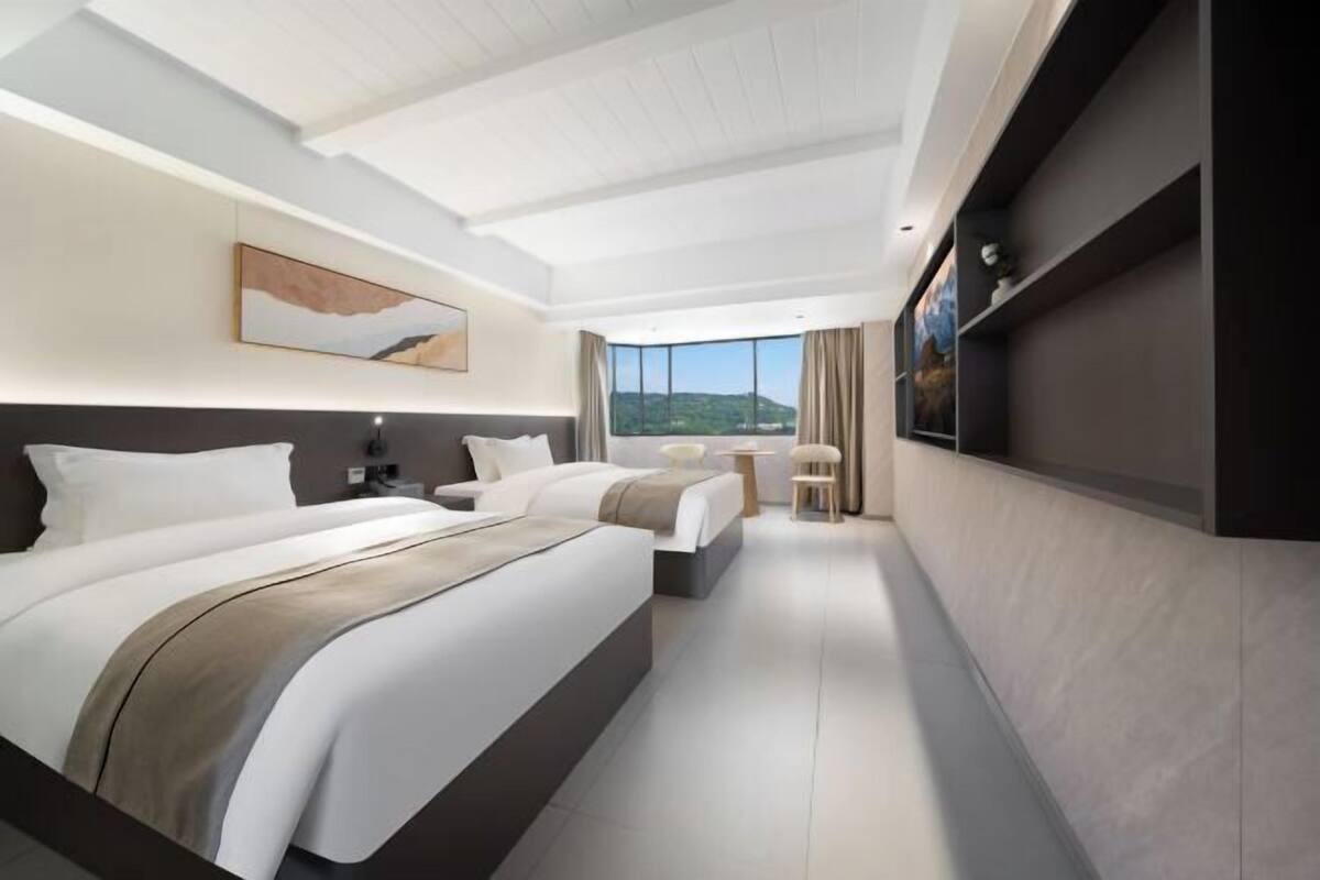 Ein modernes Hotelzimmer mit zwei Betten, einem großen Fenster und Blick ins Freie.