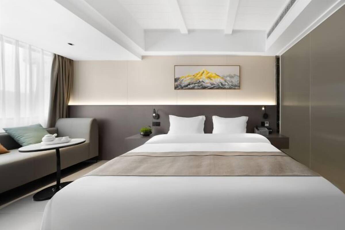Ein modernes Hotelzimmer mit einem großen Bett, einer Sitzecke, einem kleinen Tisch mit Teeservice und einem Bild an der Wand.
