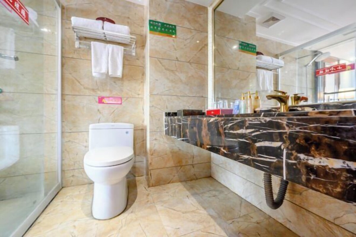 A modern bathroom with a toilet, a vanity with a black marble countertop, and a glass shower enclosure.