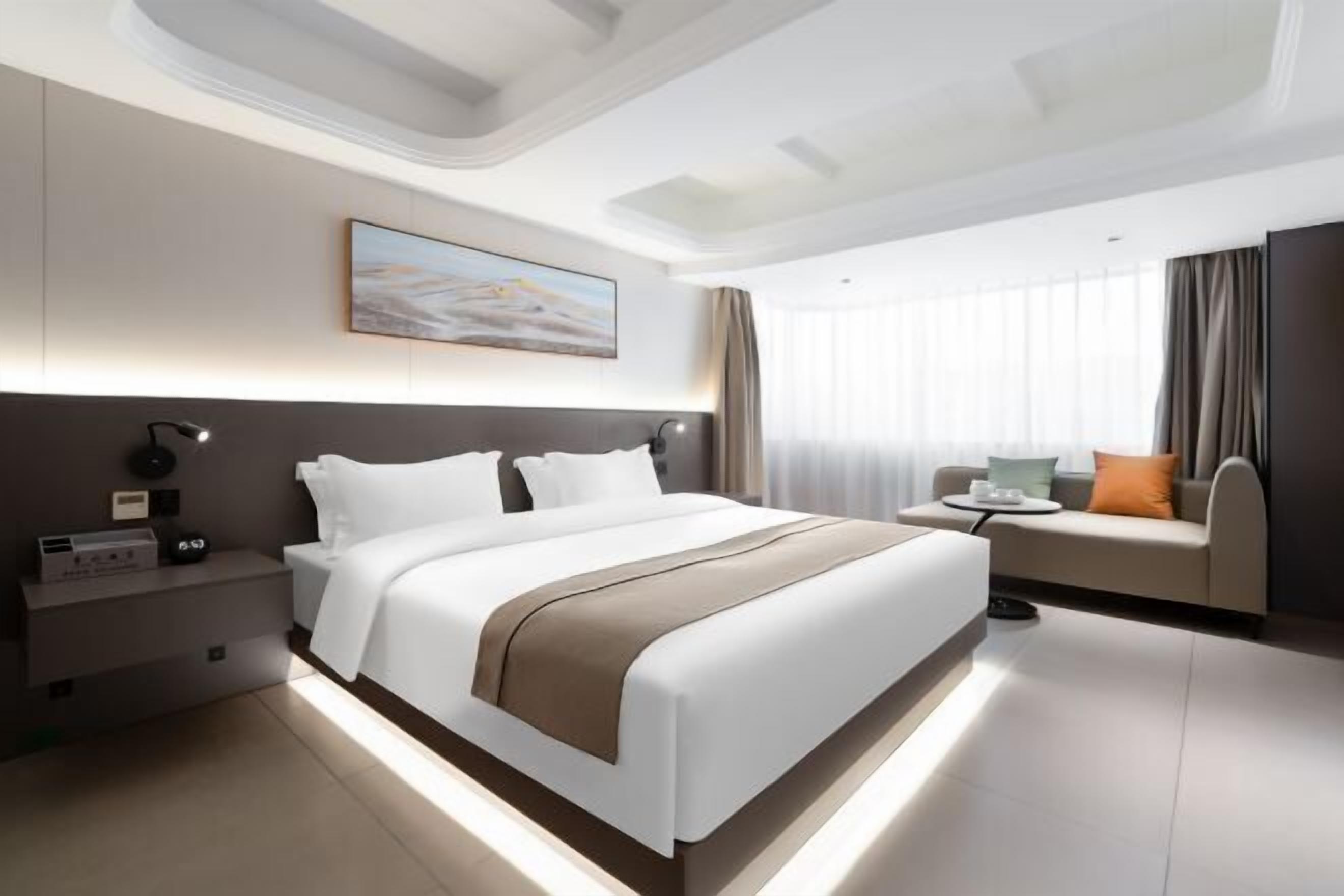 A modern hotel room with a large bed, bedside tables, a sofa, and a painting on the wall.