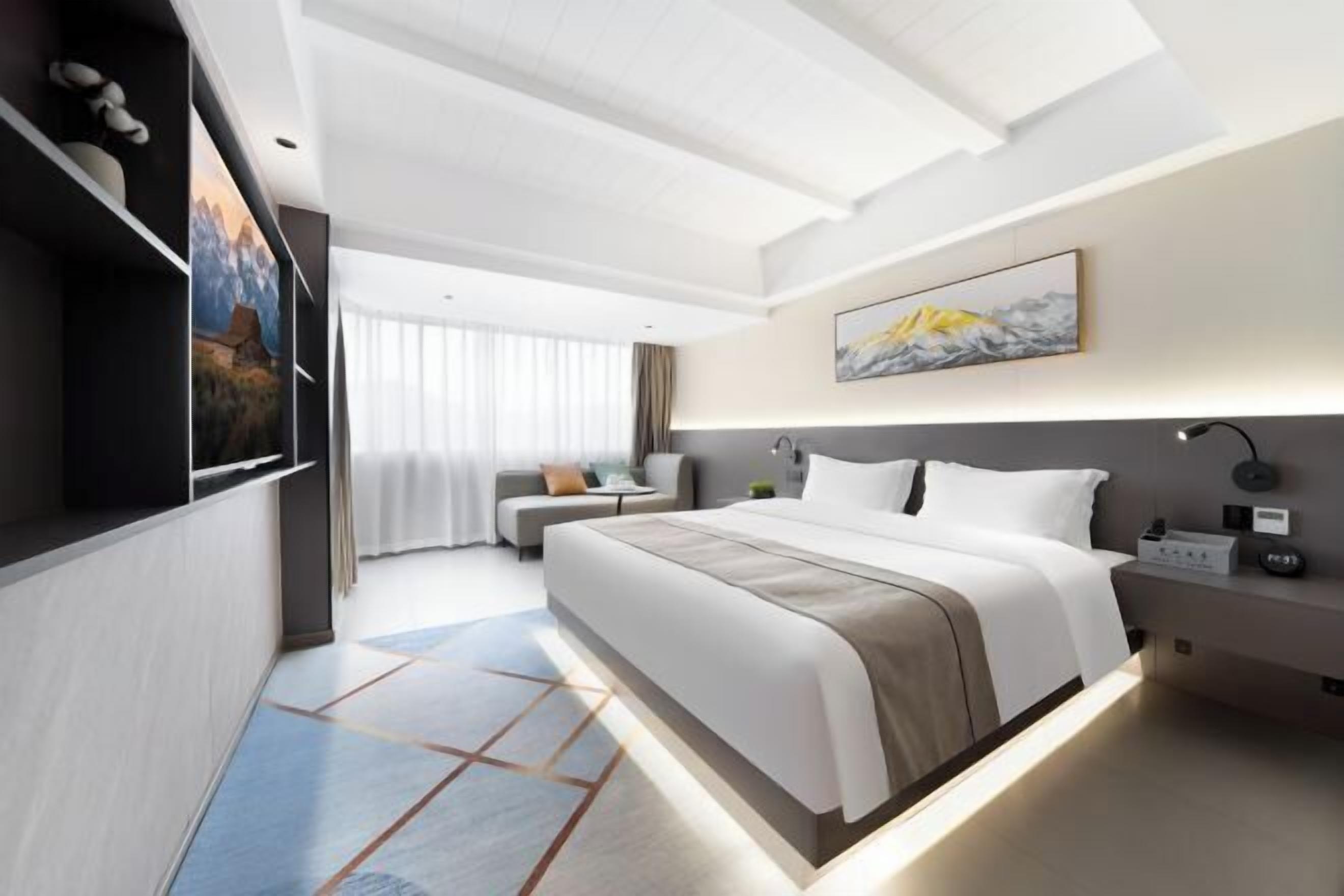 A modern hotel room with a large bed, a desk, and a sofa.