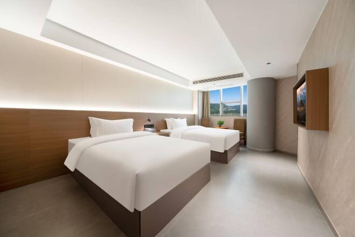 Ein modernes Hotelzimmer mit einem großen Bett, einem kleineren Bett, einem Schreibtisch und einem Fenster mit Blick.