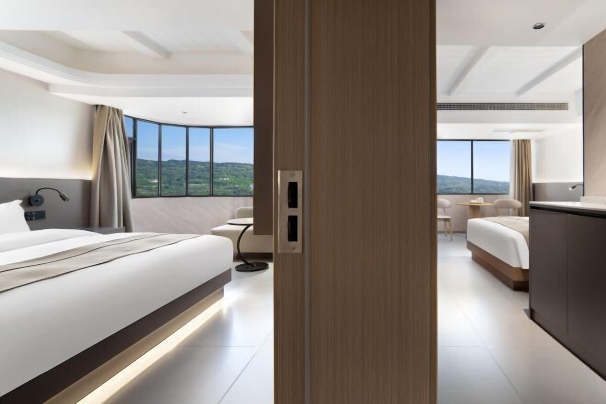 A modern hotel room with a large bed, a desk, and a view of the landscape.