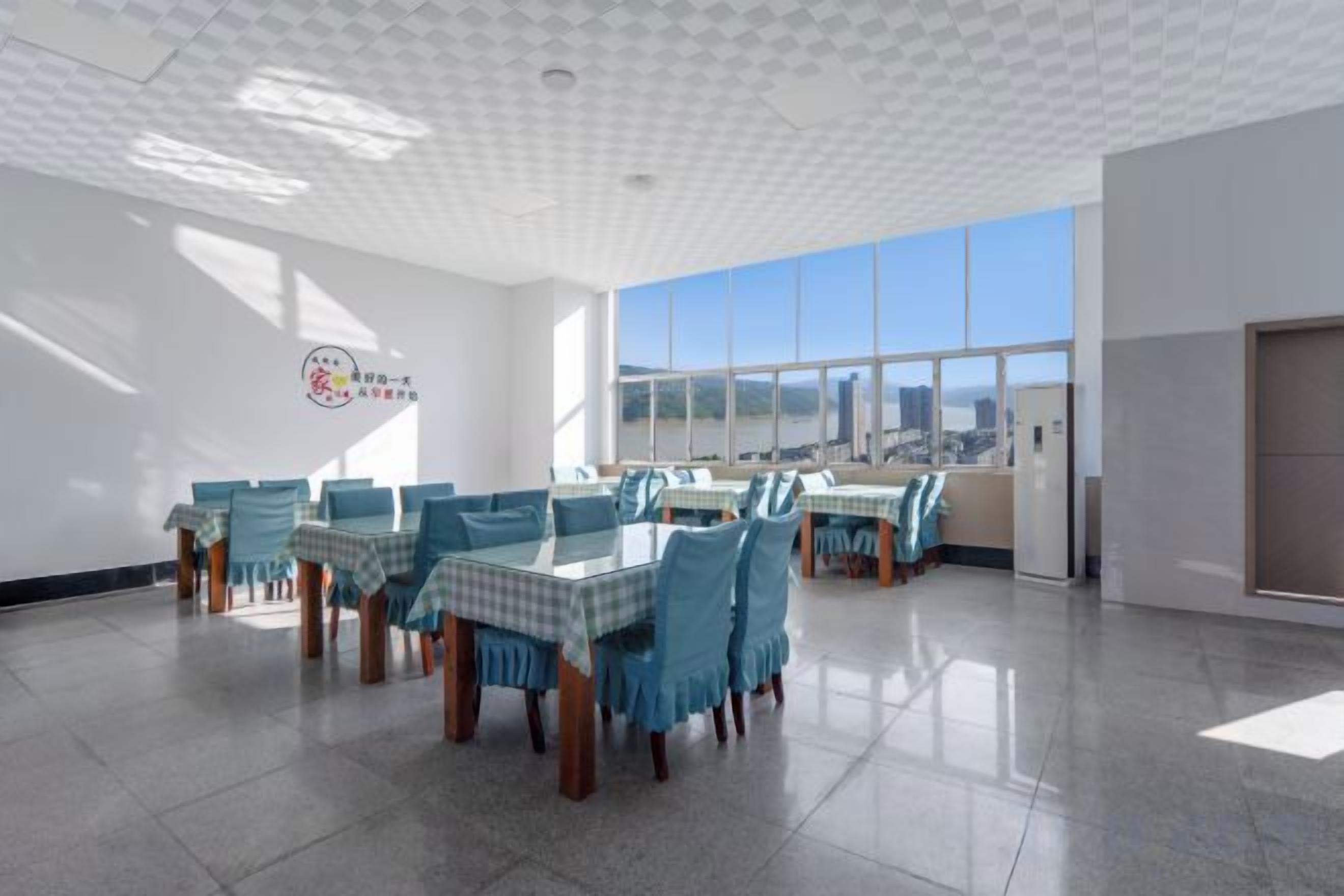A spacious room with multiple tables and chairs, large windows, and a tiled floor.