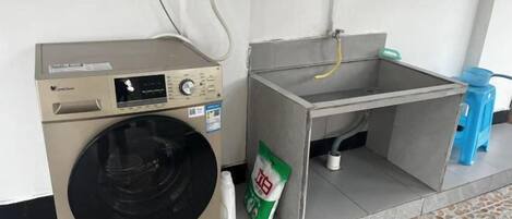 A compact laundry area with a washing machine, a sink, and a bag of detergent.