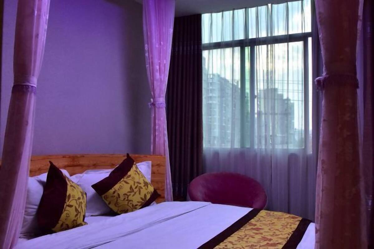 A hotel room with a bed, a chair, and a window with curtains.