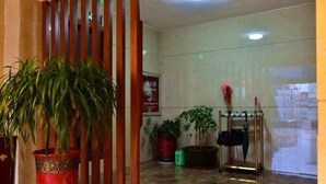 Um hall com uma grande planta em vaso, um painel de madeira, um suporte de guarda-chuvas e um chão em azulejos.