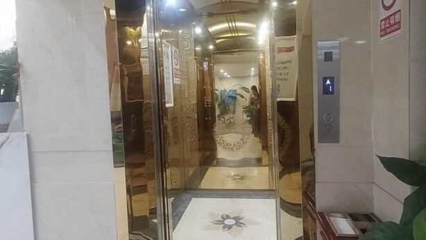 Entrada de elevador com porta de vidro, placa de proibido fumar e botão do elevador.