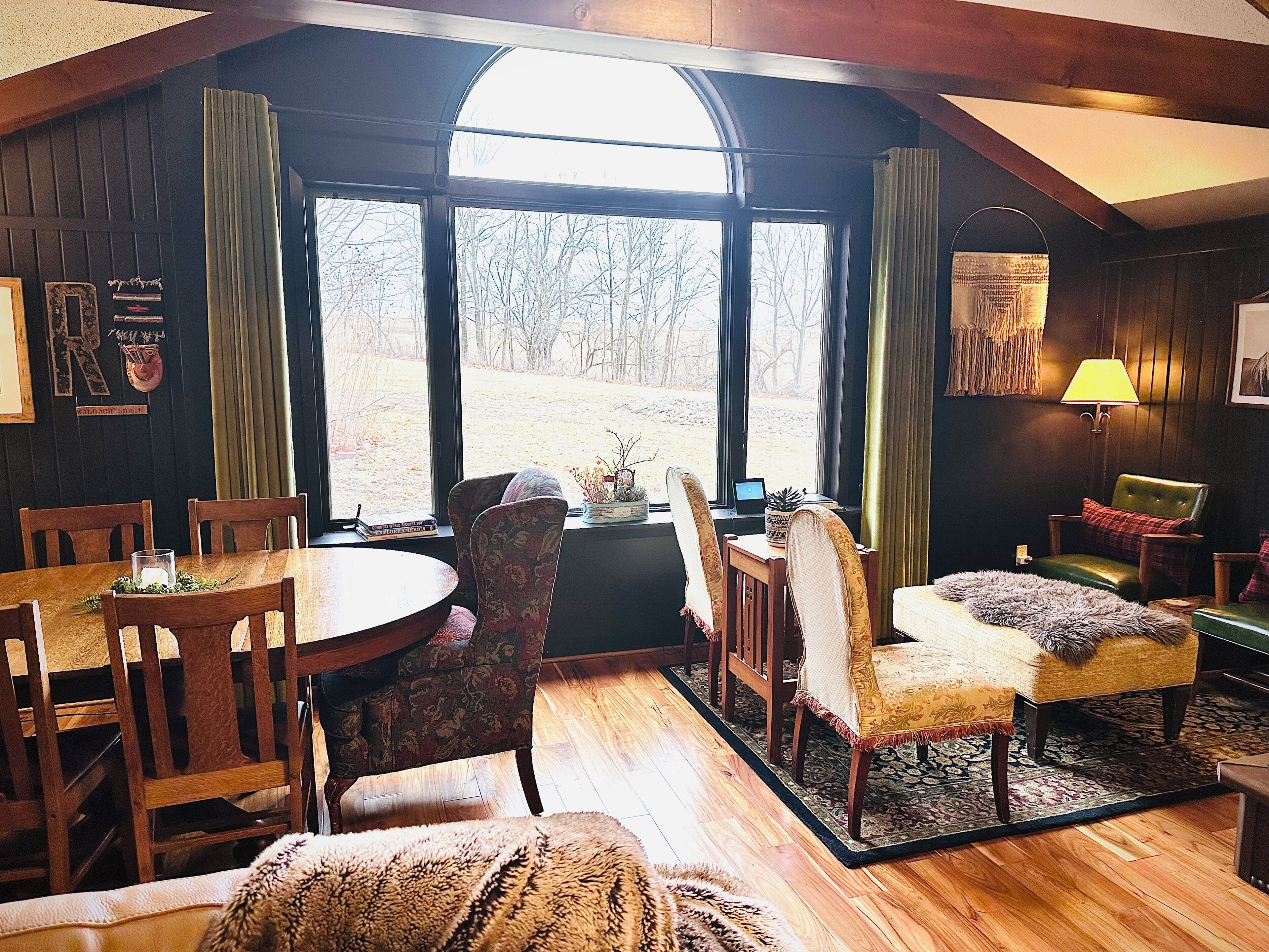 A cozy room with a large window, wooden furniture, and a lamp.