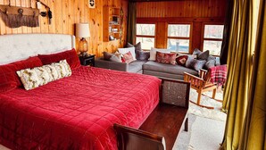 Ein gemütliches Cabin-Zimmer mit einem großen Bett, einer Couch und einem Sessel. Es gibt einen Deckenventilator, eine Lampe und ein Fenster mit Vorhängen.