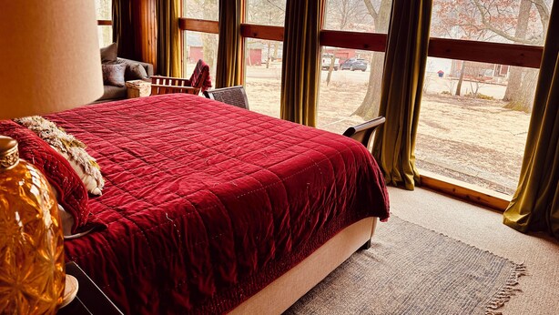 Ein Schlafzimmer mit einem großen Bett, einem Sessel und einem Fenster mit Vorhängen.