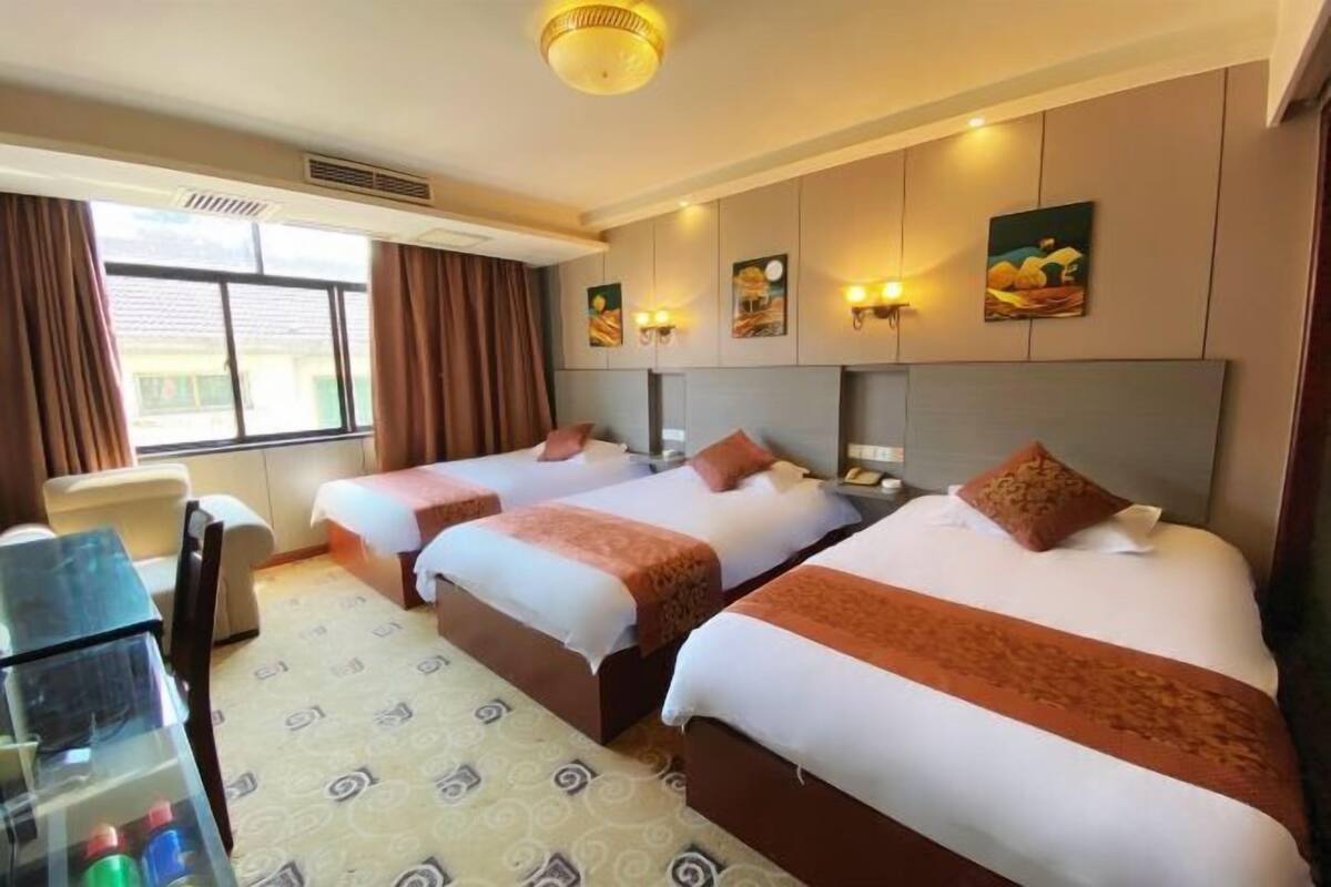 A hotel room with three beds, a desk, and a window with curtains.