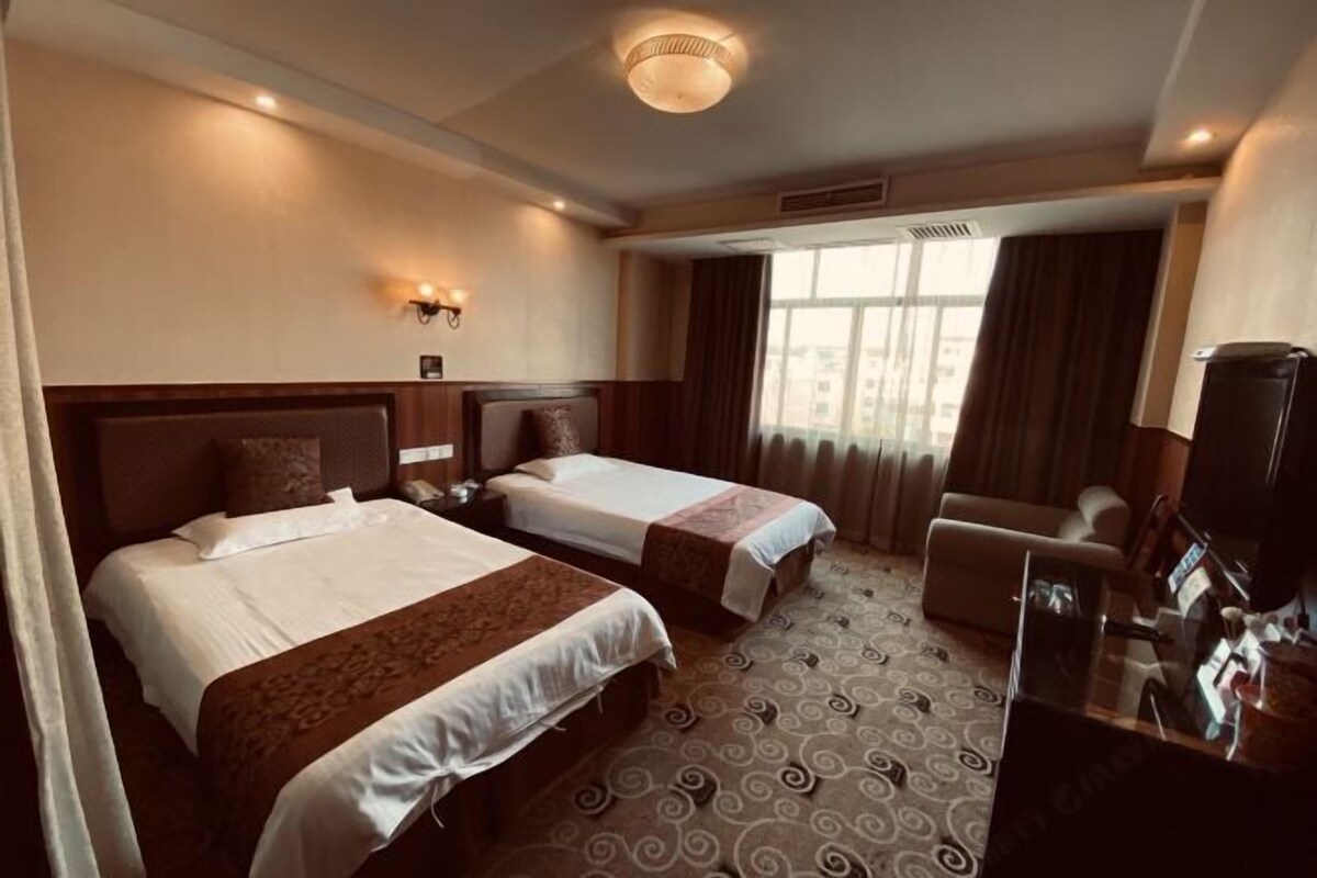 A hotel room with two beds, a sofa, a TV, and a window with curtains.