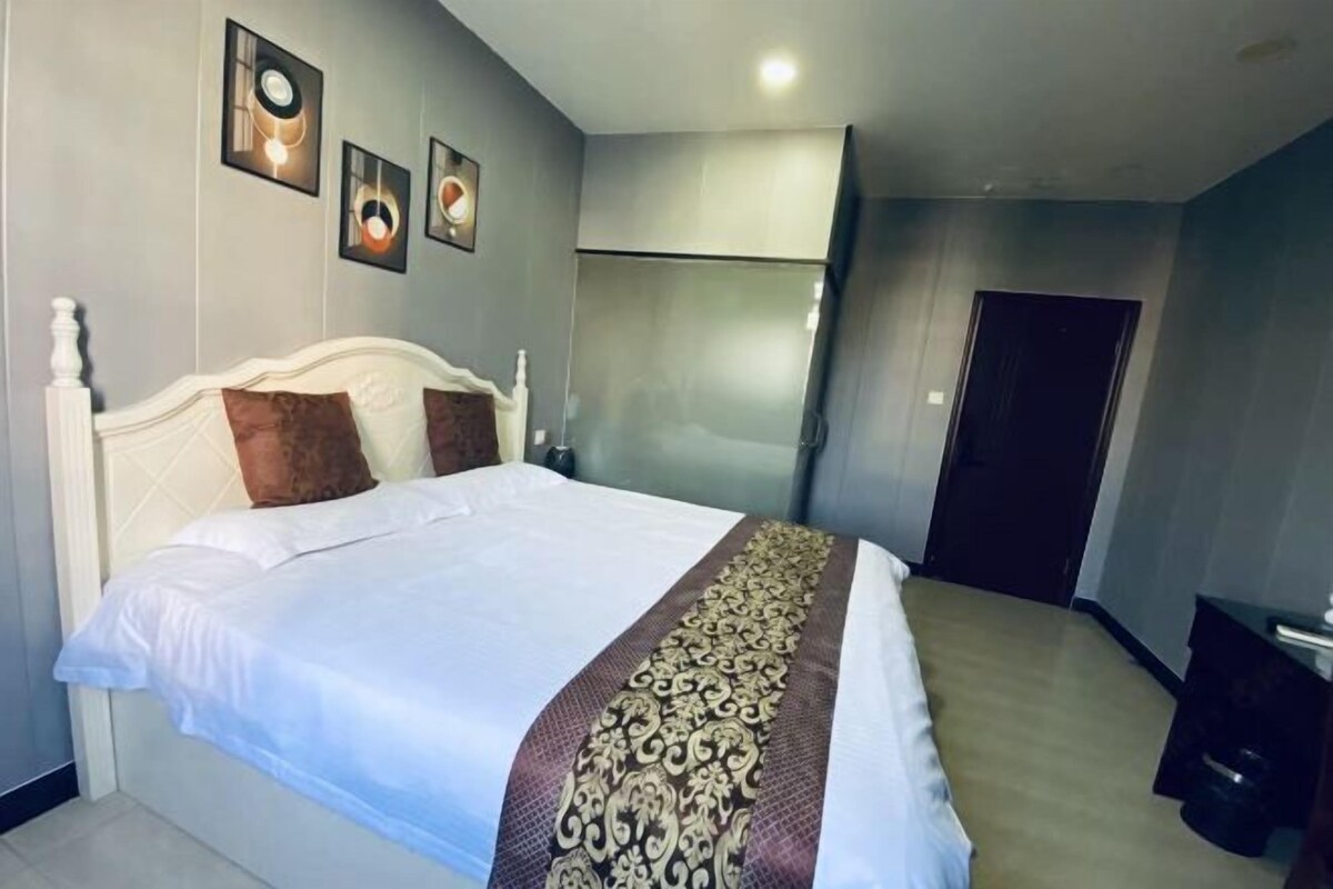 A neatly made bed with a white headboard and decorative pillows, a bedside table with a lamp, and a wall-mounted artwork above the bed.