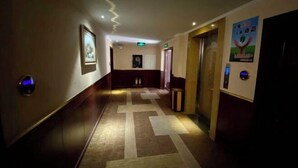 A hotel hallway with a patterned carpet, framed artwork on the walls, and an elevator. - Jinshang Haoting Hotel (Wuyi)