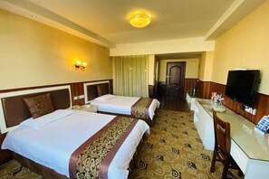 A hotel room with two beds, a desk, a television, and a door leading to a hallway.