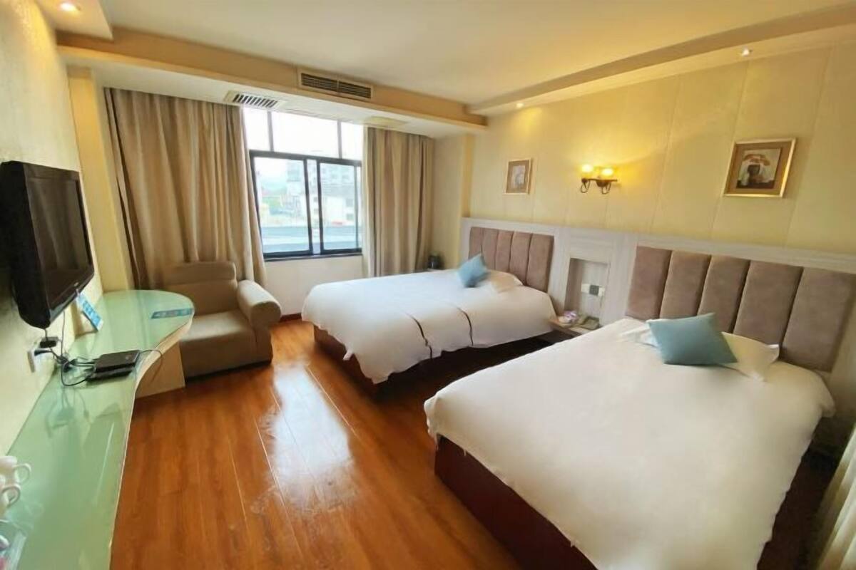 A hotel room with two beds, a desk with a computer, a TV, and a window with curtains.