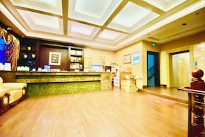 A hotel lobby with a reception desk, a staircase, and a reception area.