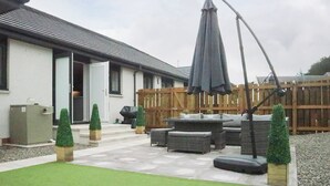 Un patio con mobiliario exterior, cerca de madera y un edificio con fachada blanca.