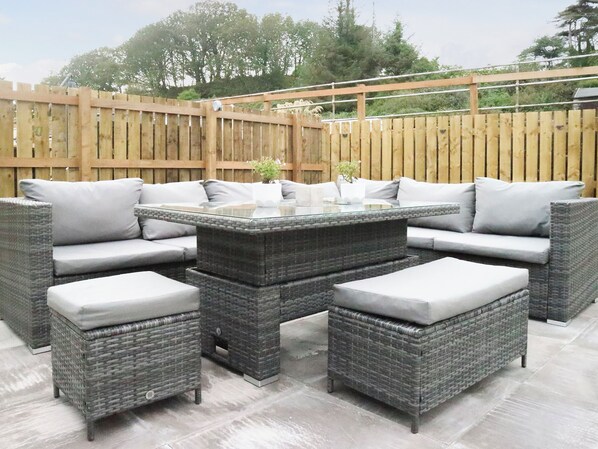 An outdoor patio with wicker furniture, a glass-top table, and a wooden fence.