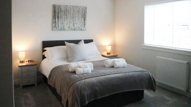 Un dormitorio con una cama, dos lámparas de noche, un ventanal con persianas, un radiador y una obra de arte colgada en la pared.