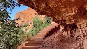 A set of concrete steps leading up a rocky hillside, surrounded by sparse vegetation and a large rock formation overhead.