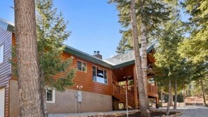 A two-story log cabin with a covered porch and a gravel driveway.