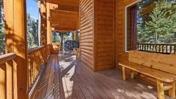 A wooden cabin with a porch, a bench, and a view of trees.