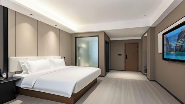 A modern hotel room with a large bed, a nightstand, a TV, and a door leading to another room. - Chibi Lake Holiday Hotel (Xinjiekou Commercial Street) (Chibi)