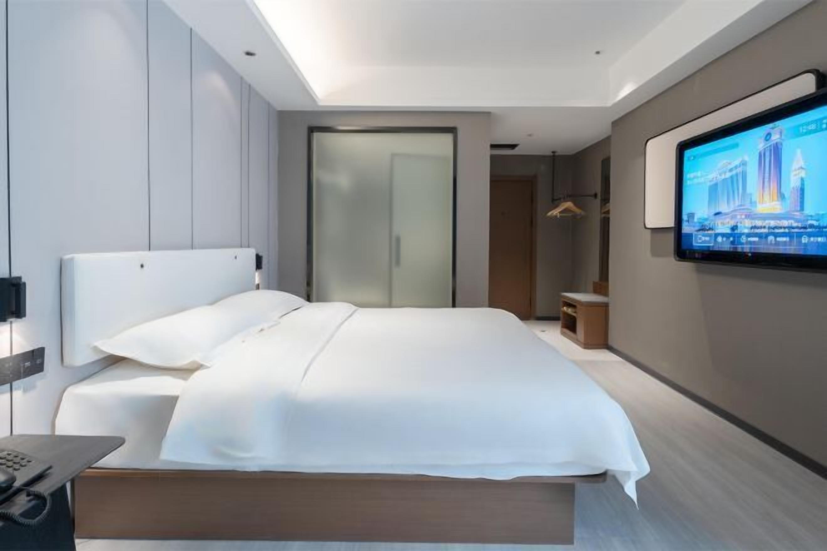 Ein modernes Hotelzimmer mit einem großen Bett, einem an der Wand befestigten Fernseher und einem Nachttisch mit Telefon.