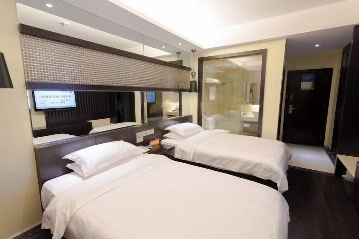 Hotellihuone, jossa on kaksi sänkyä, suuri peili, televisio ja kylpyhuone, joka on näkyvissä lasiovesta.
