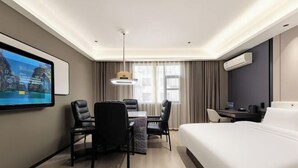 A hotel room with a bed, desk, chairs, a TV, and an air conditioning unit. - Chibi Lake Holiday Hotel (Xinjiekou Commercial Street) (Chibi)