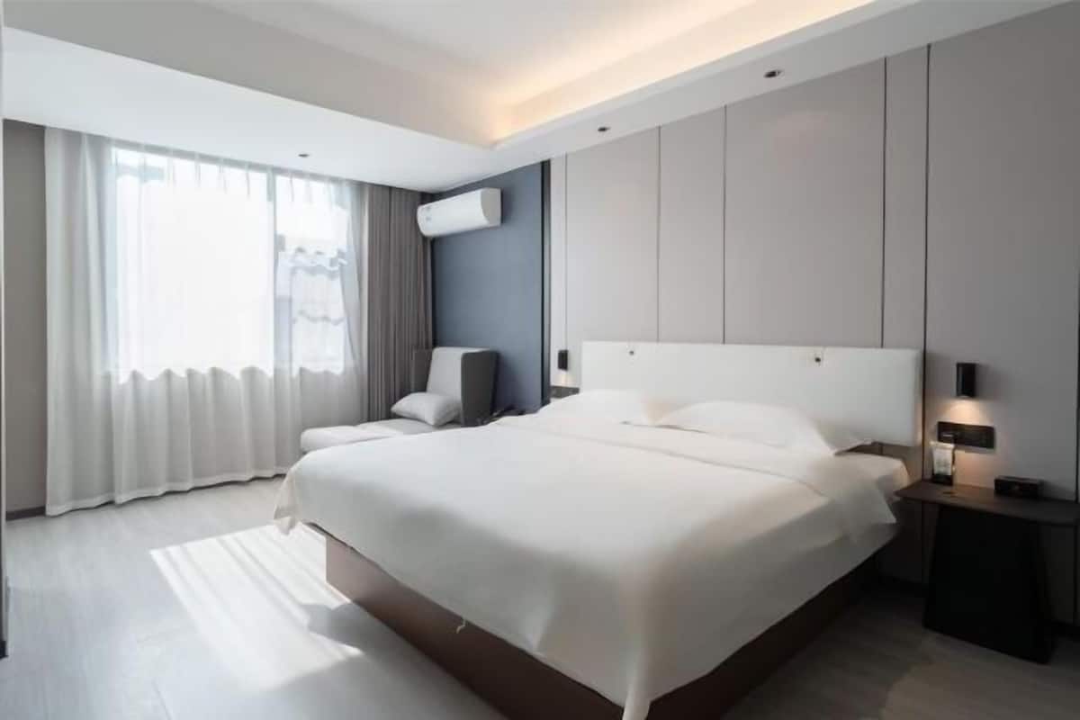 Moderni hotellihuone, jossa on suuri sänky, yöpöytä, tuoli ja ikkuna, jossa on verhot.