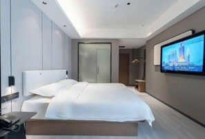 A modern hotel room with a large bed, a flat-screen TV mounted on the wall, and a desk with a telephone.