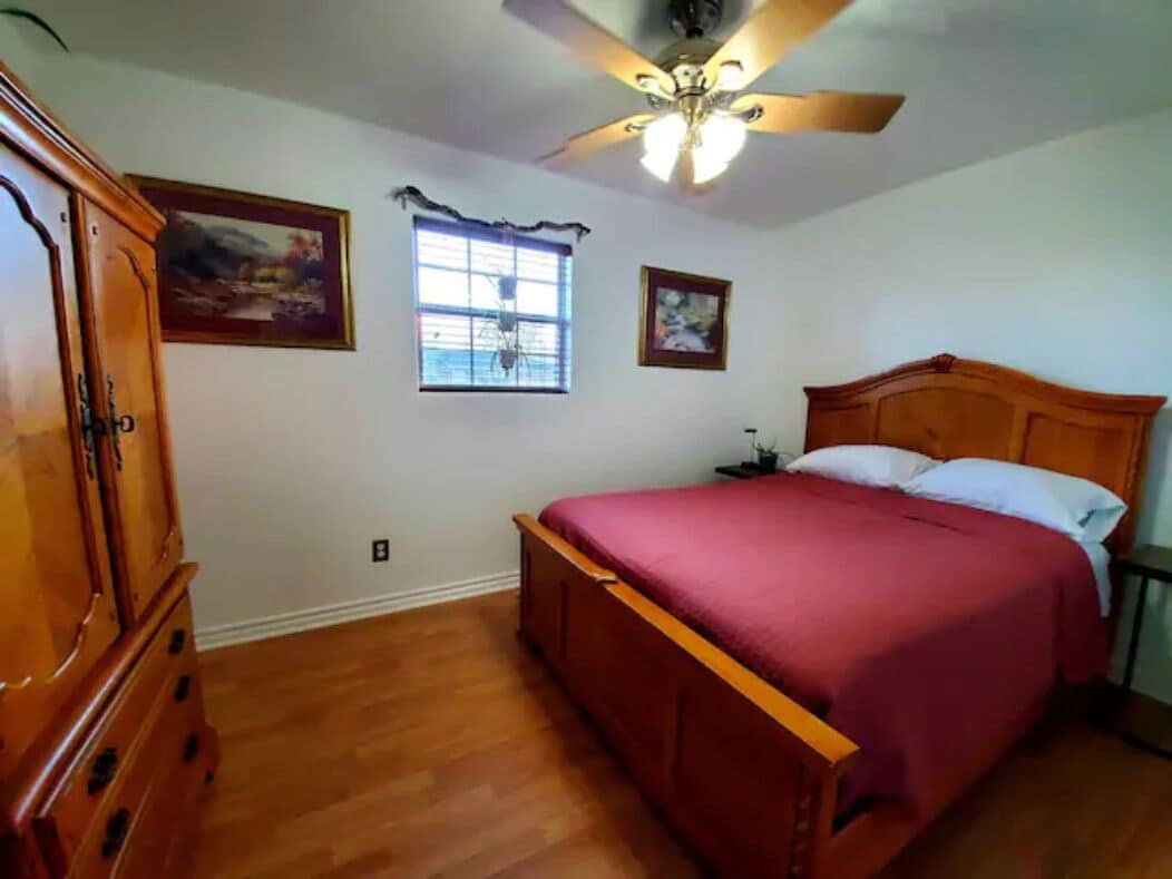 Un dormitorio con una cama de madera, un ventilador de techo y dos cuadros en la pared.