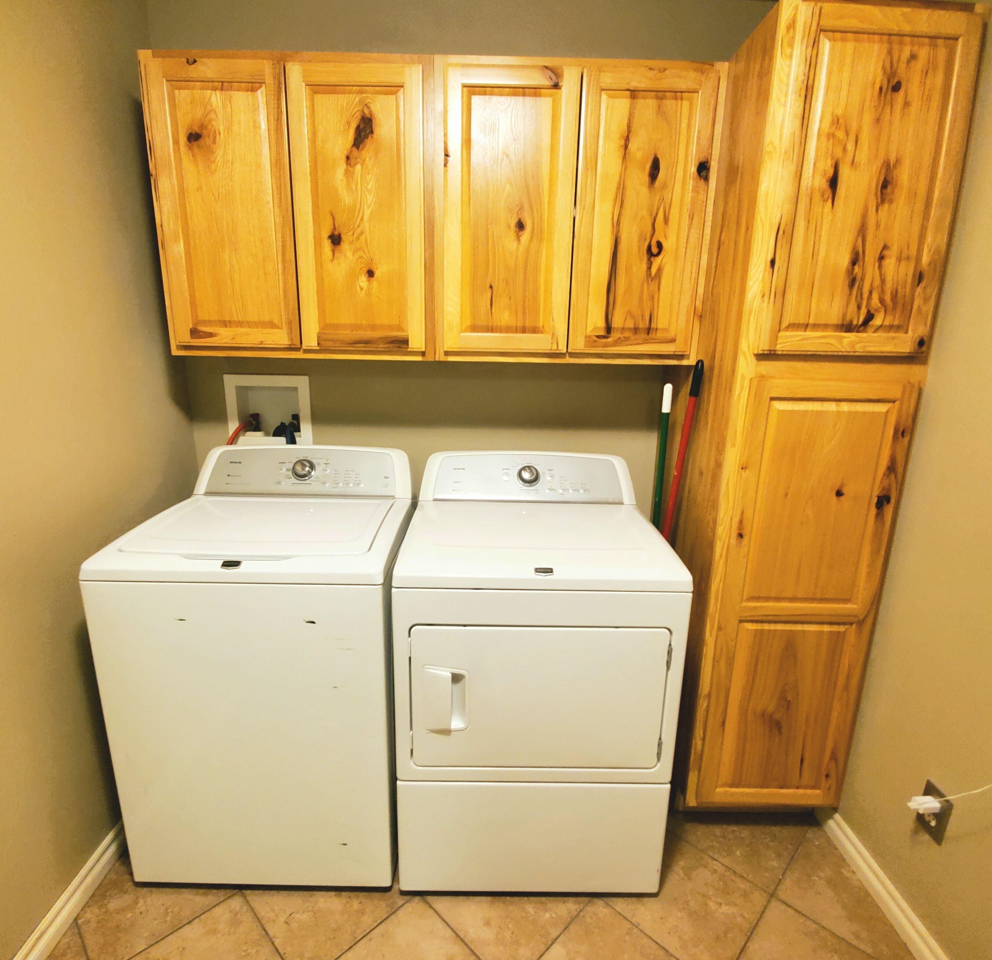A laundry room with two white front-loading washers and wooden cabinets above.