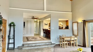 A spacious living area with a high ceiling, a dining area with wooden chairs and a table, and a kitchen visible through an open doorway. - Private Forest Cabin with Wrap-Around Deck, Fireplaces & Unlimited Hiking (Payson)