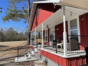 A red building with a white porch, steps leading to the porch, and outdoor furniture. - Little Red Lake House (Greers Ferry)