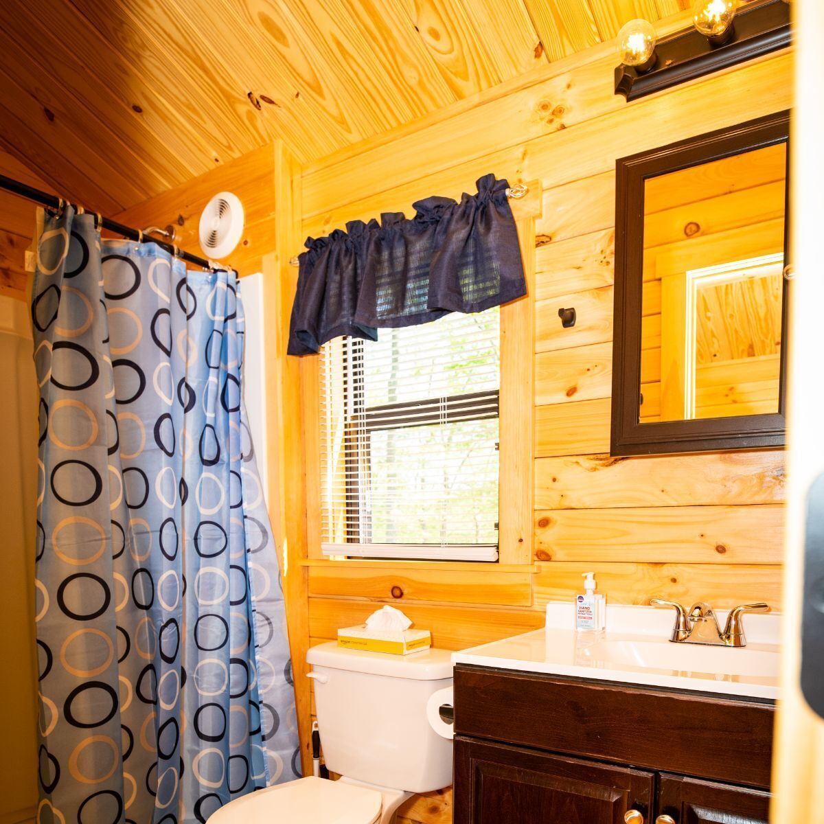 A wooden cabin bathroom with a toilet, sink, and mirror.