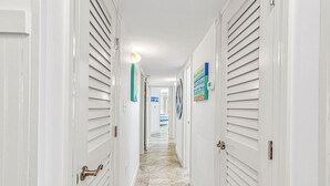 A hallway with white doors, a stone floor, and a ceiling light. - 3 Bed/3 Bath ~ 2nd Floor Oceanfront Prime Condo ~ Elevator ~ 1205 Queens Court (Emerald Isle)