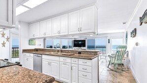 A kitchen with white cabinets, granite countertops, and a view of the ocean. - 3 Bed/3 Bath ~ 2nd Floor Oceanfront Prime Condo ~ Elevator ~ 1205 Queens Court (Emerald Isle)