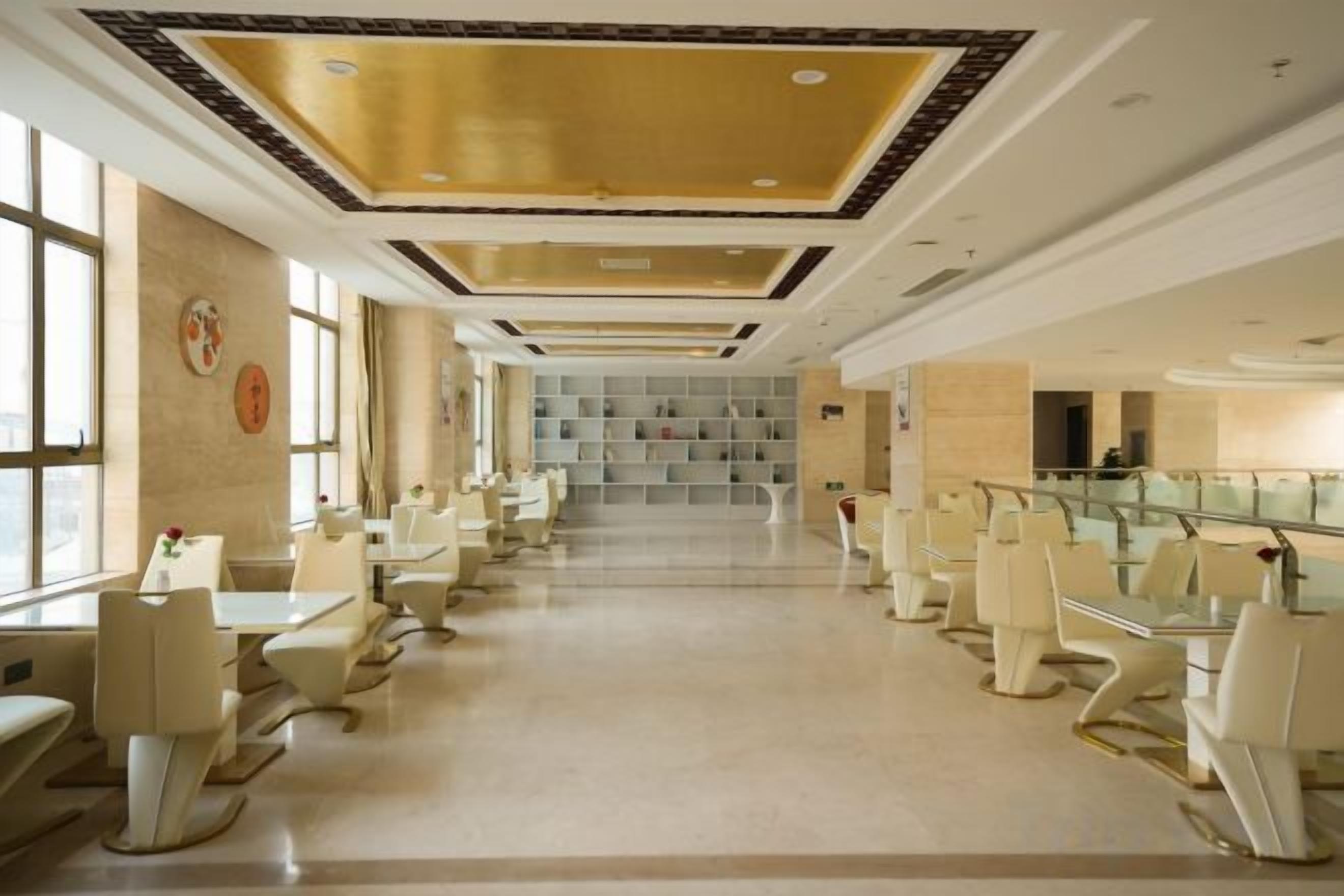 A spacious hotel lobby with a long row of seating, a central staircase, and a modern ceiling design.