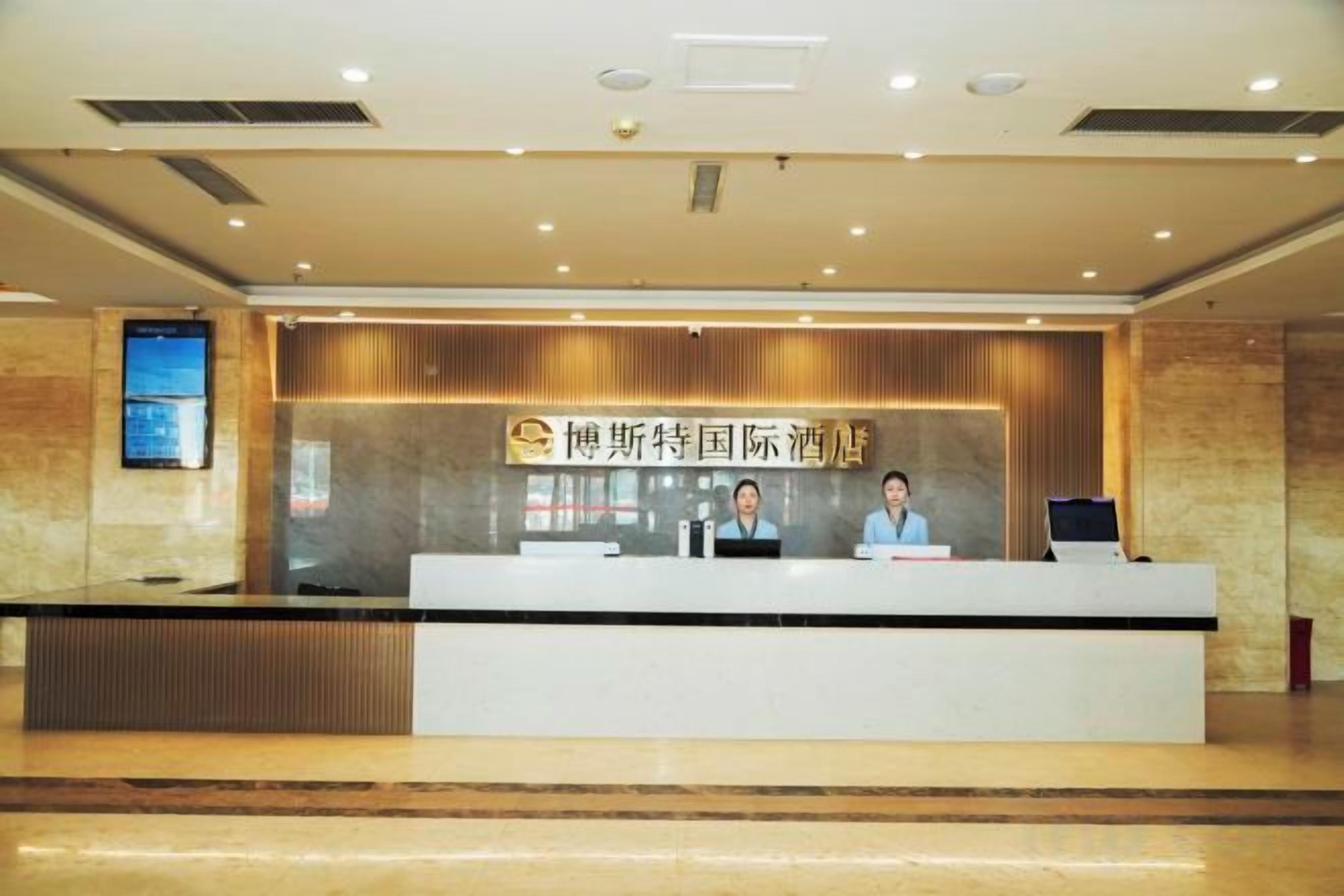 A reception desk with a sign, two staff members, and a digital screen.