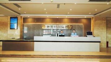 A reception desk with a sign, two staff members, and a digital screen.